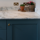 Antique brass Barlow Furniture Knob on a teal cabinet adds elegance to the kitchen décor.