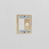 Antique brass slimline plate for 25mm module & 1G switch, shown without cover on a white textured wall.