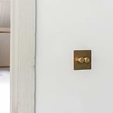 Antique brass 2G two way dimmer switch fixed to off white wall next to off white wooden door panel
