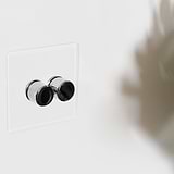Clear polished nickel 2G two way dimmer switch fixed to white wall with shadow of plant to the right