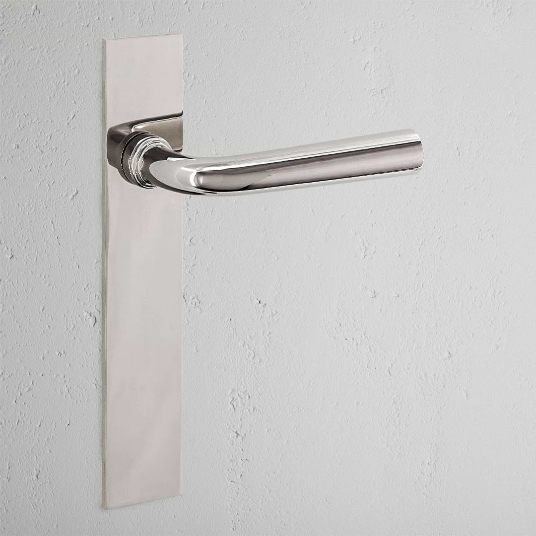 Apsley Long Plate Fixed Door Handle in polished nickel on a textured white wall.