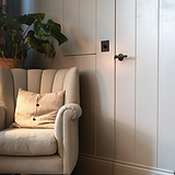 Bronze 1g two way dimmer switch fixed to cream wooden slatted wall with cream armchair to the left and plant behind