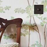 Bronze toggle switch against wallpapered wall with wooden chair