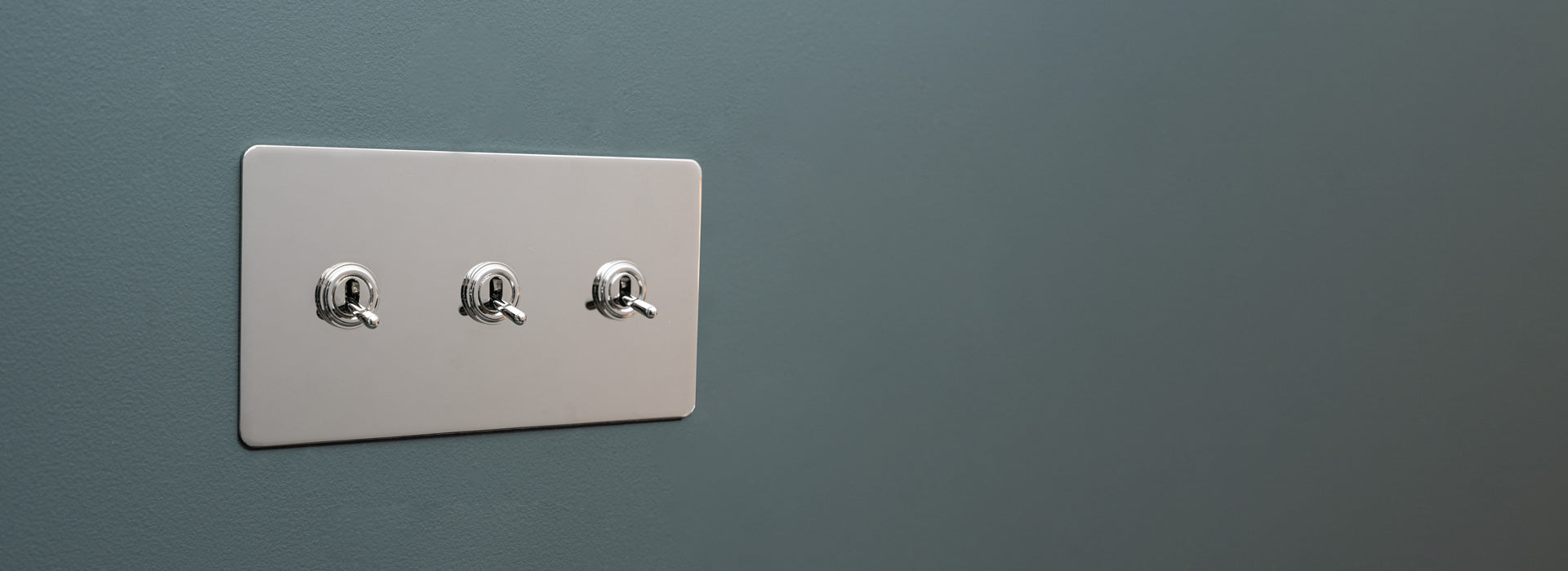 Nickel-Schalter mit drei Kipphebeln an einer grauen Wand