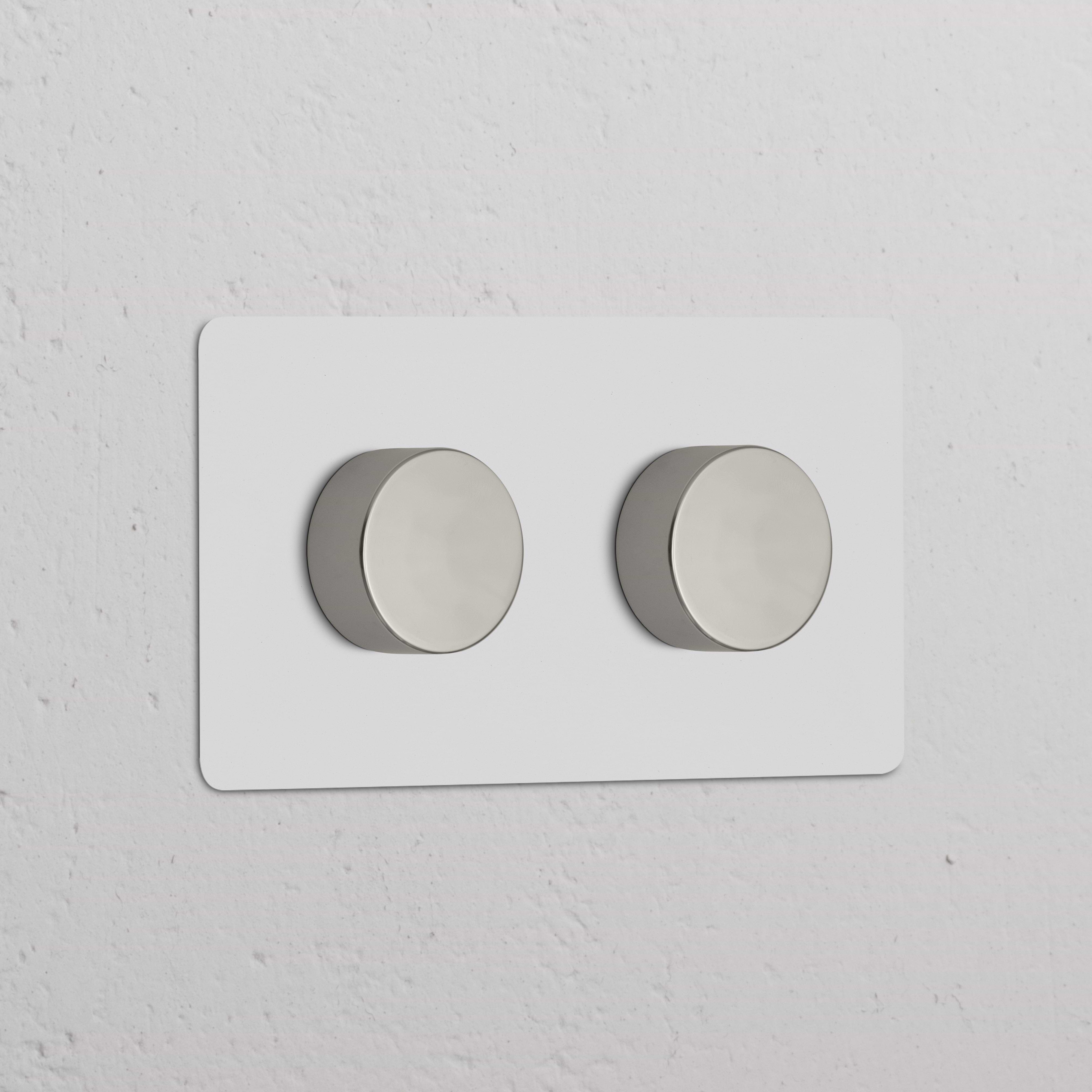 Zweifachrahmen mit 2x Mehrpunkt-Dimmerschalter, lackierbar und poliertes Nickel, an weißer Wand montiert.