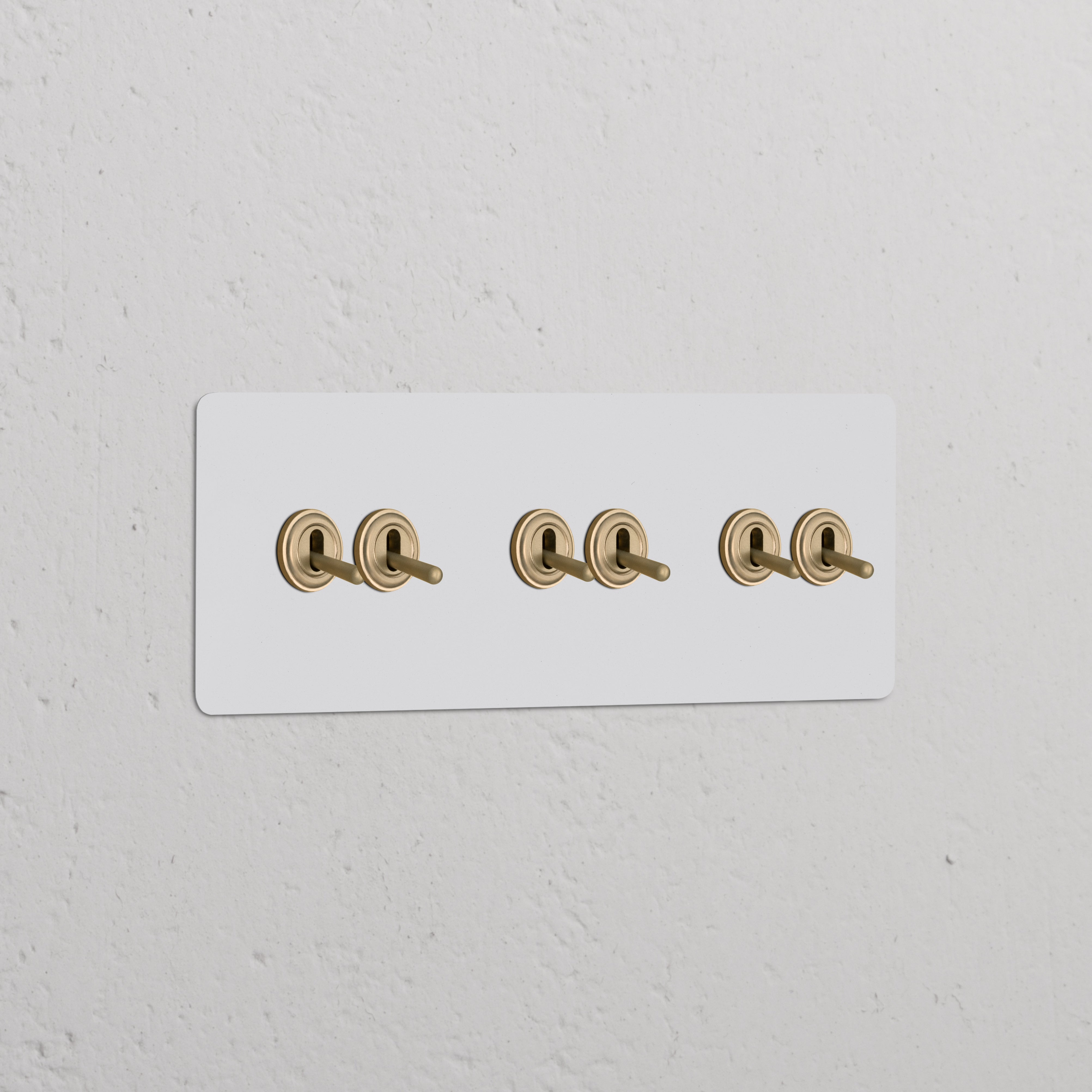 Dreifachrahmen mit 6 Kipphebelschaltern, lackierbar, in Antikmessing auf weißer Wand. Zur Individualisierung geeignet.