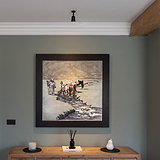 Baylis Einzelstrahler 50 mm – Bronze – an eine weiße Decke montiert, Licht fällt von oben herab auf ein gerahmtes Kunstwerk, das an einer Wand über einem hölzernen Konsole-Tisch befestigt ist. 