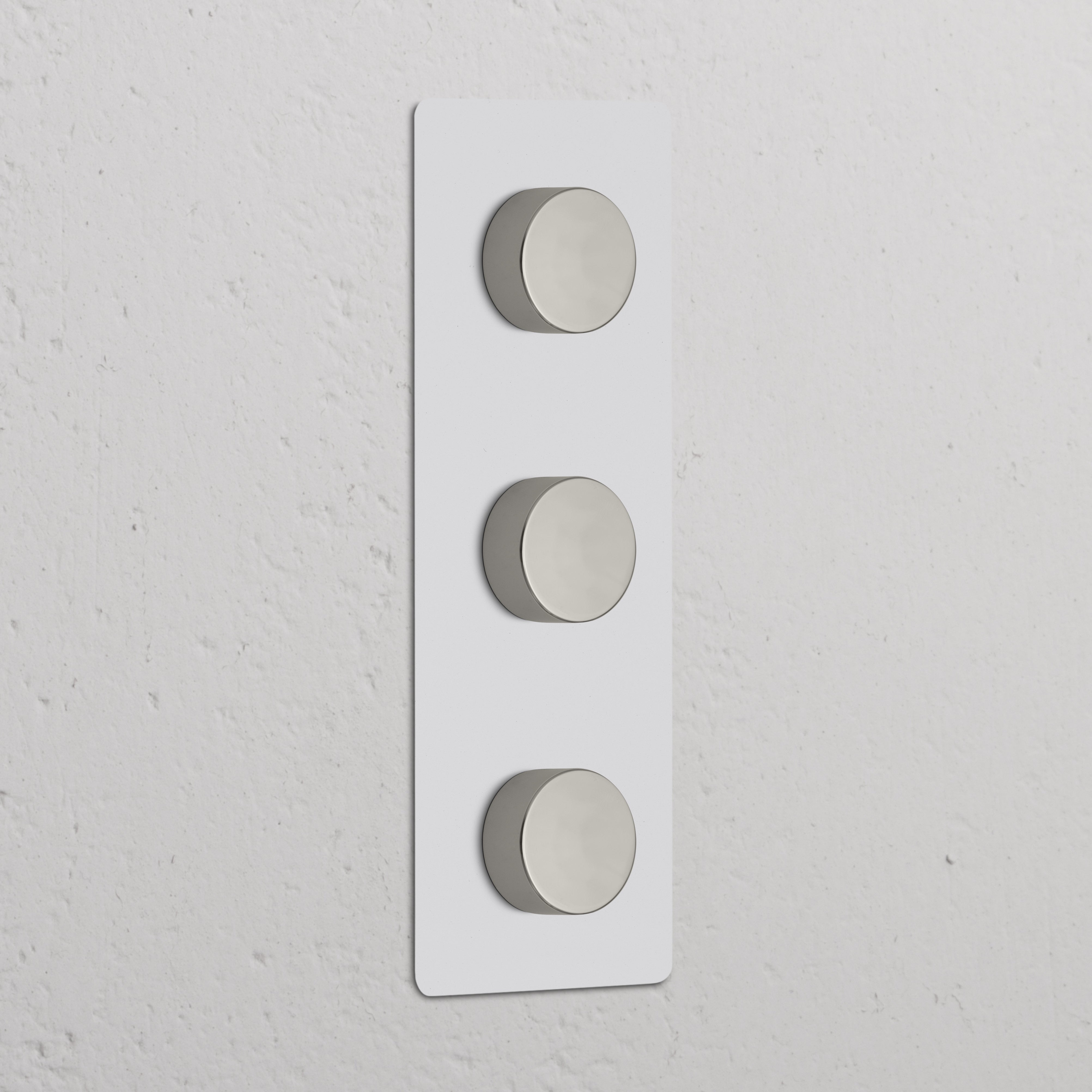 Vertikaler Dreifachrahmen mit 3x Mehrpunkt-Dimmerschalter, lackierbar und poliertes Nickel, an Wand montiert.