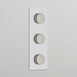Vertikaler Dreifachrahmen mit 3x Mehrpunkt-Dimmerschalter, lackierbar und poliertes Nickel, an Wand montiert.