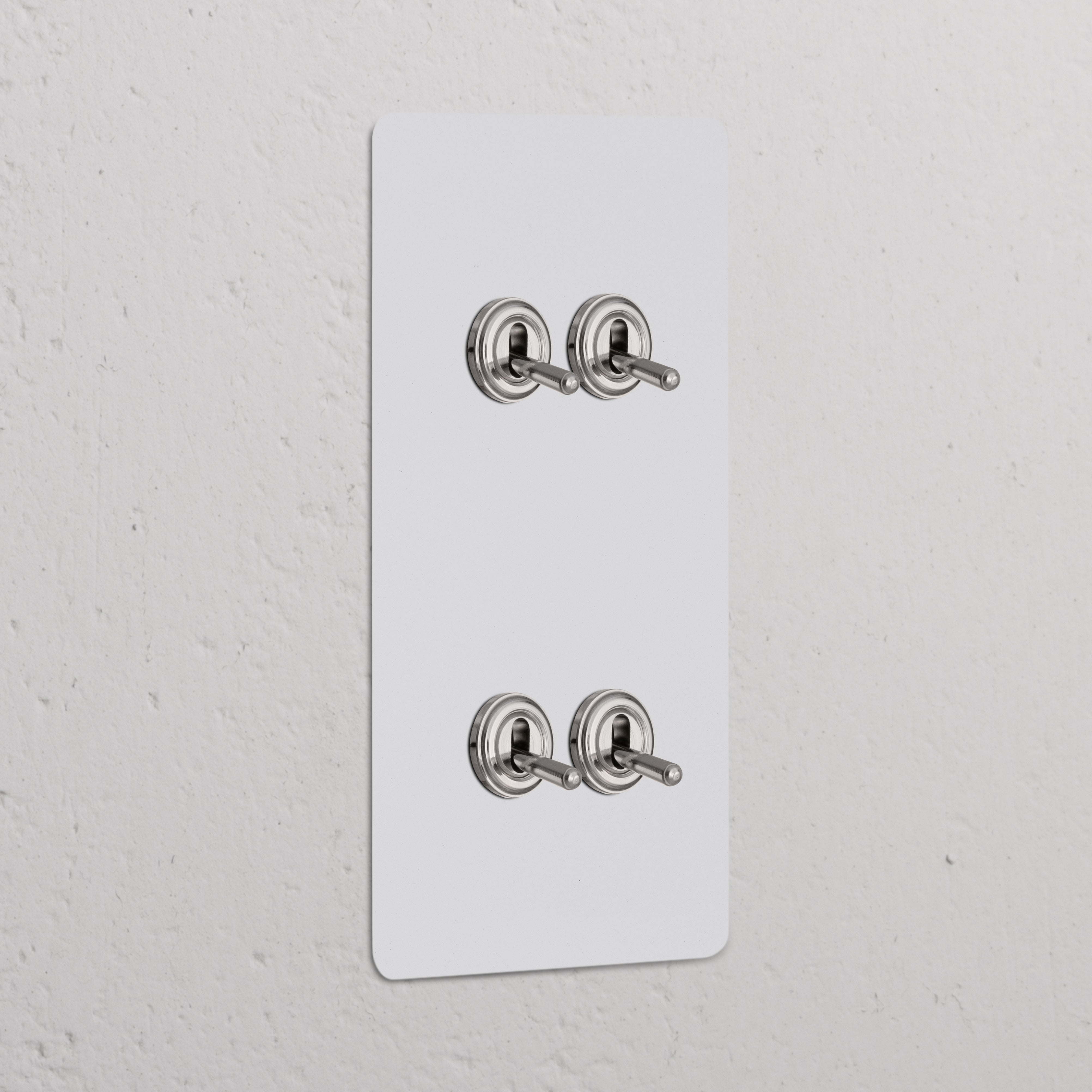 Vertikaler Zweifachrahmen mit 4x Kipphebelschalter, lackierbar, poliertes Nickel, an einer Wand montiert.