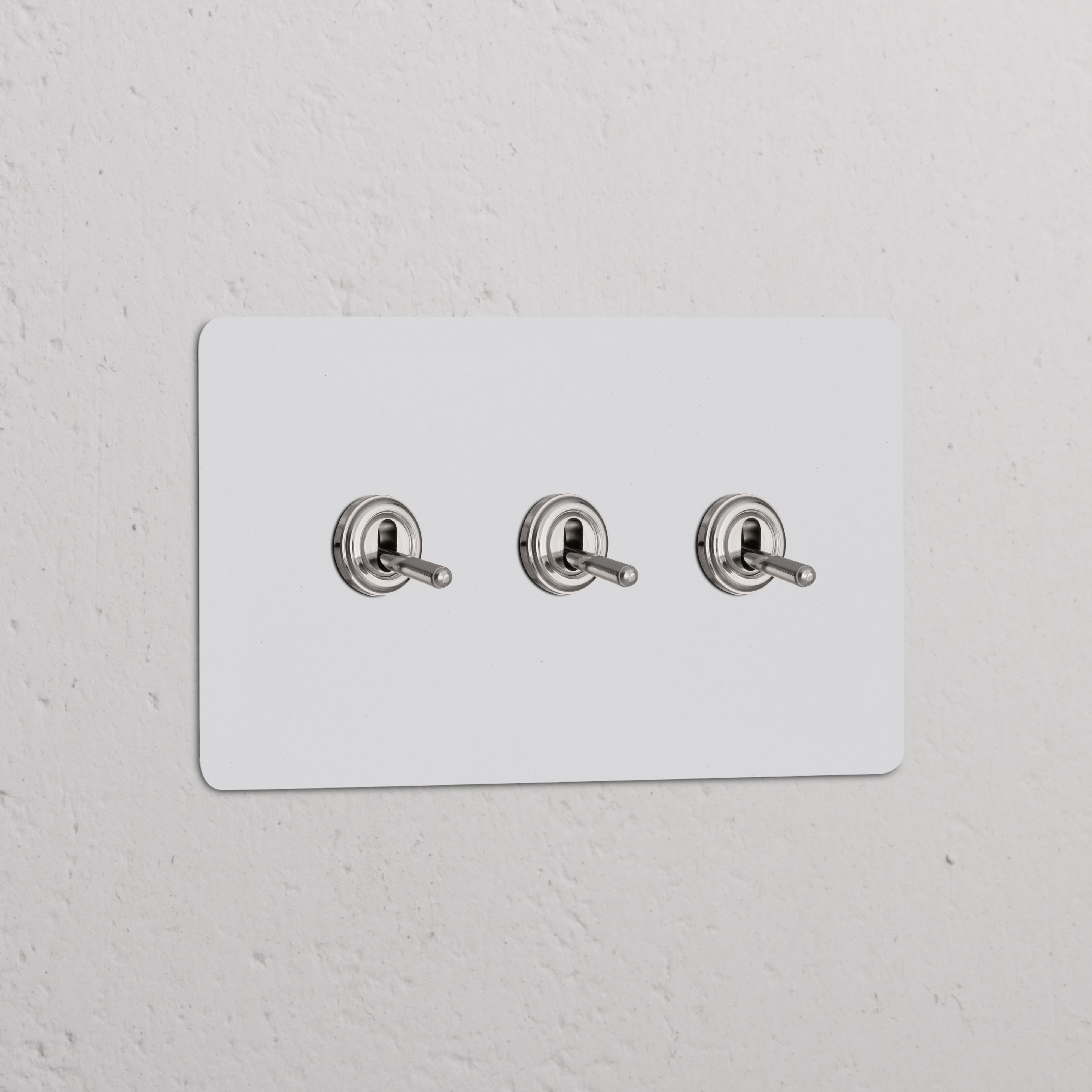 Zweifachrahmen mit 3x Kipphebelschalter, lackierbar, poliertes Nickel, auf weißem Wandpaneel.