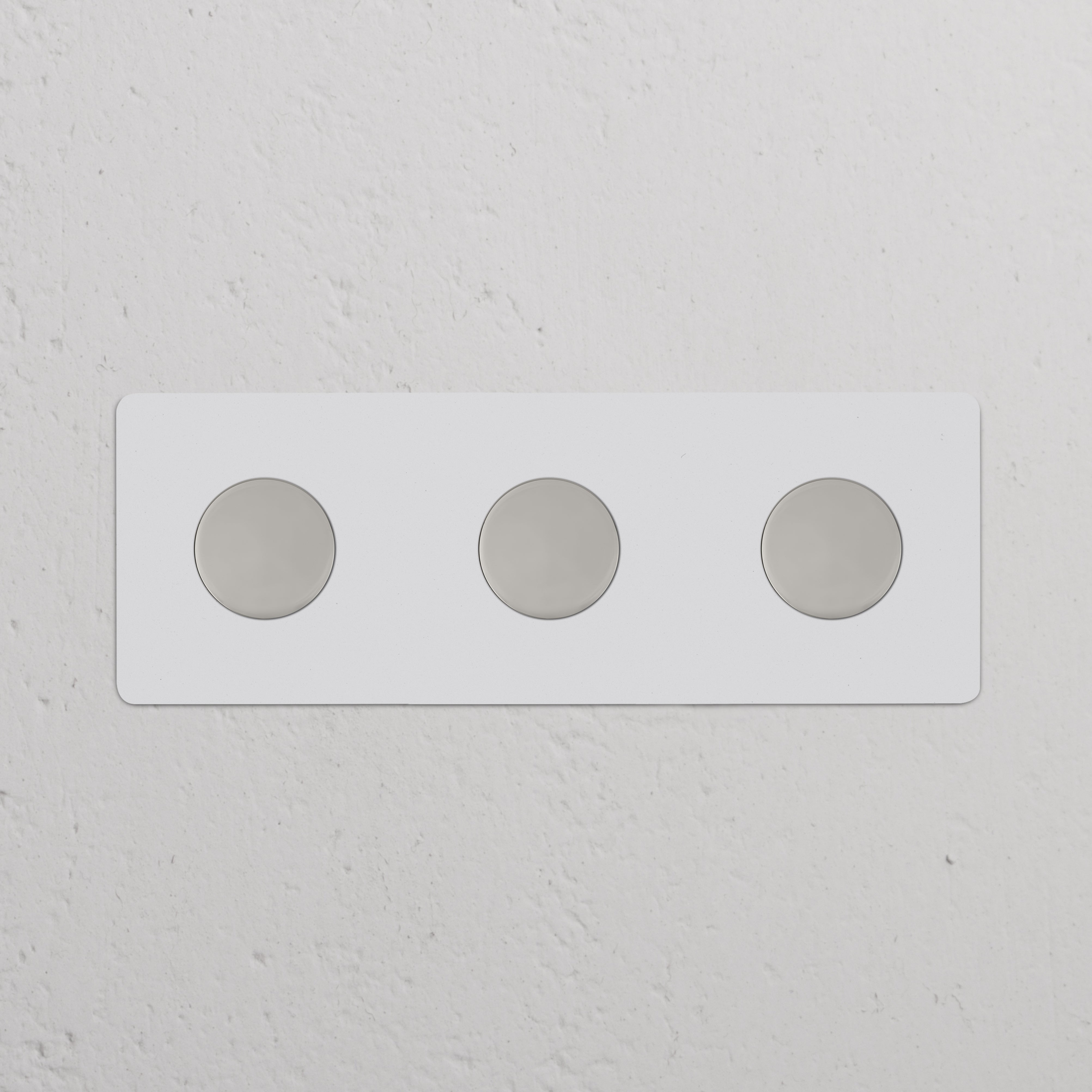Dreifachrahmen mit 3x Mehrpunkt-Dimmerschalter, lackierbar mit poliertem Nickel, an weißer Wand montiert.