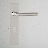 Manilla para puerta con placa larga Apsley en níquel pulido, con cerradura europea y muelle, montada en pared blanca.