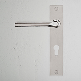 Manilla para puertas Apsley, níquel pulido con placa larga y cerradura europea, en una pared blanca texturizada.