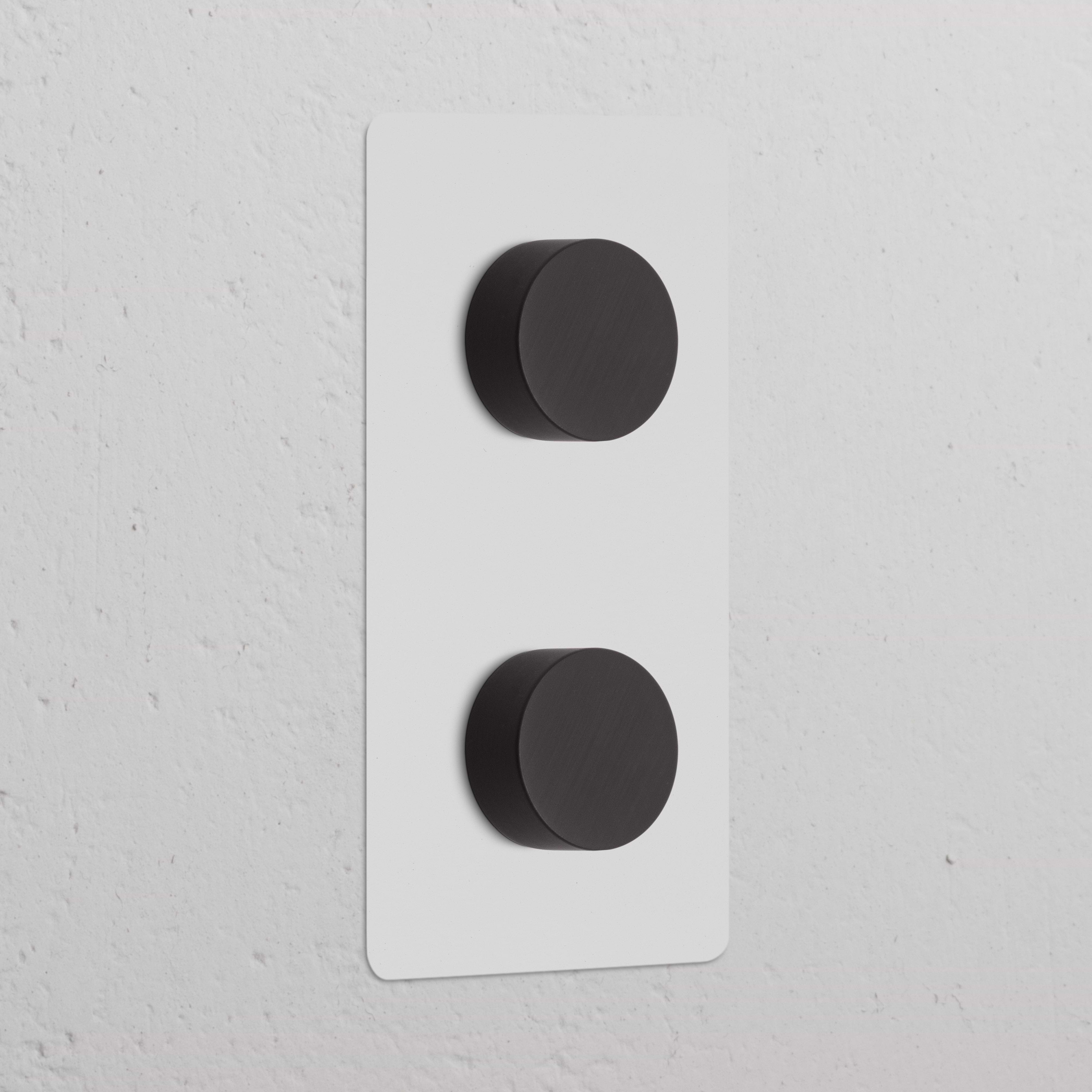 Reguladores de intensidad de luz verticales en marco doble, pintable y acabado bronce, sobre pared blanca texturizada.