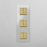 Solución superior de control de luces: Interruptor triple de balancín en latón antiguo y traslúcido con blanco con seis posiciones en diseño vertical sobre fondo blanco