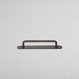 Tirador estilo manija para muebles Kilburn en bronce sobre fondo blanco