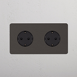 Tomas Schuko dobles en marco de bronce doble con inserto negro, diseñadas para una funcionalidad elegante.