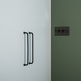 Tirador para mueble de bronce sicómoro, 224 mm, sobre puertas de armario blancas al lado de una pared verde oscuro.