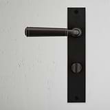 Manilla para puertas Digby con placa larga y sistema giratorio en bronce sobre puerta negra.