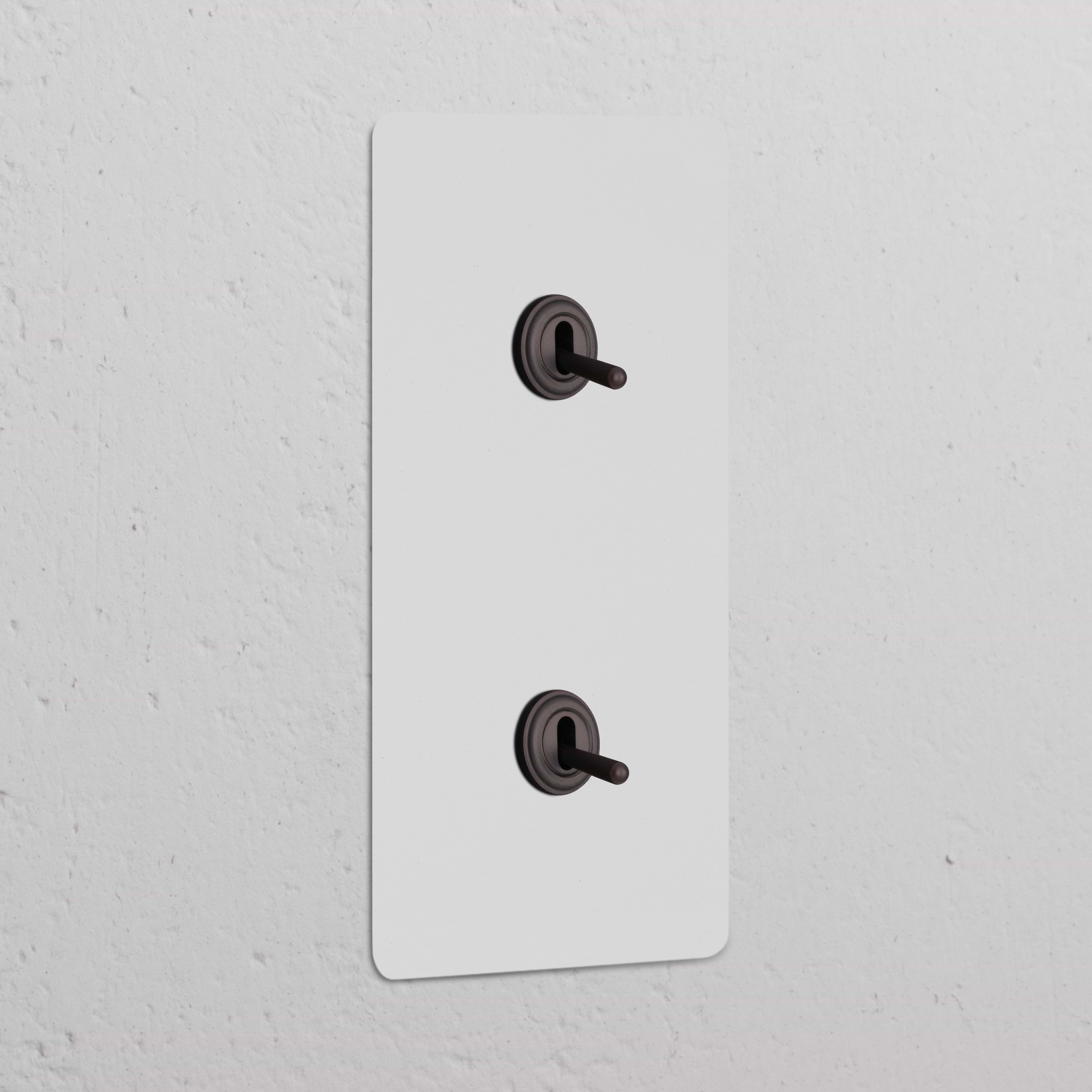 Interruptor conmutador de palanca x2 vertical en marco doble, pintable y bronce, ideal para control de luz.
