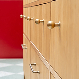 Tirador redondo Bayswater colocado en múltiples puertas de mueble de madera con pared roja y piso de mosaicos.