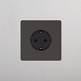 Base Schuko redonda en marco de bronce con inserto negro, adecuada para instalación de un solo módulo en la pared.