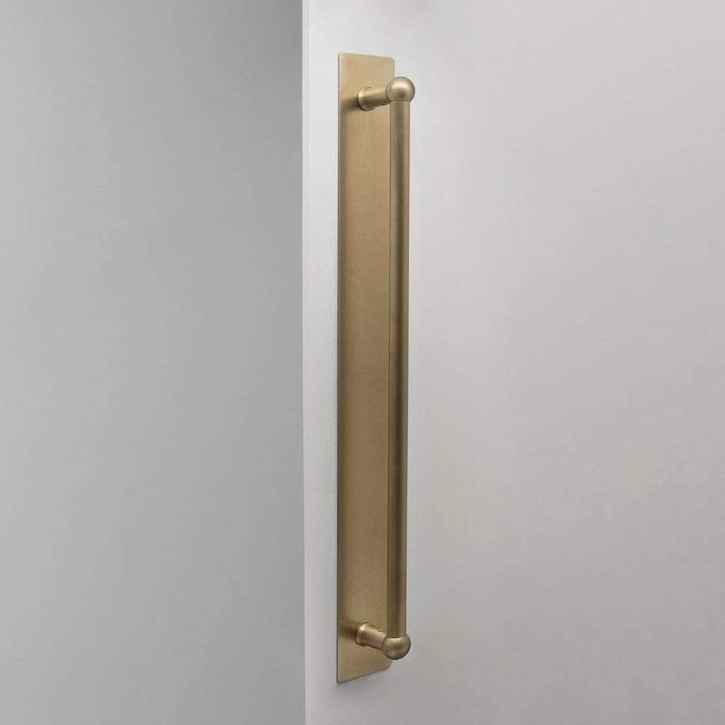 Tirador simple para puertas Harper con placa en latón antiguo de 500mm sobre fondo blanco