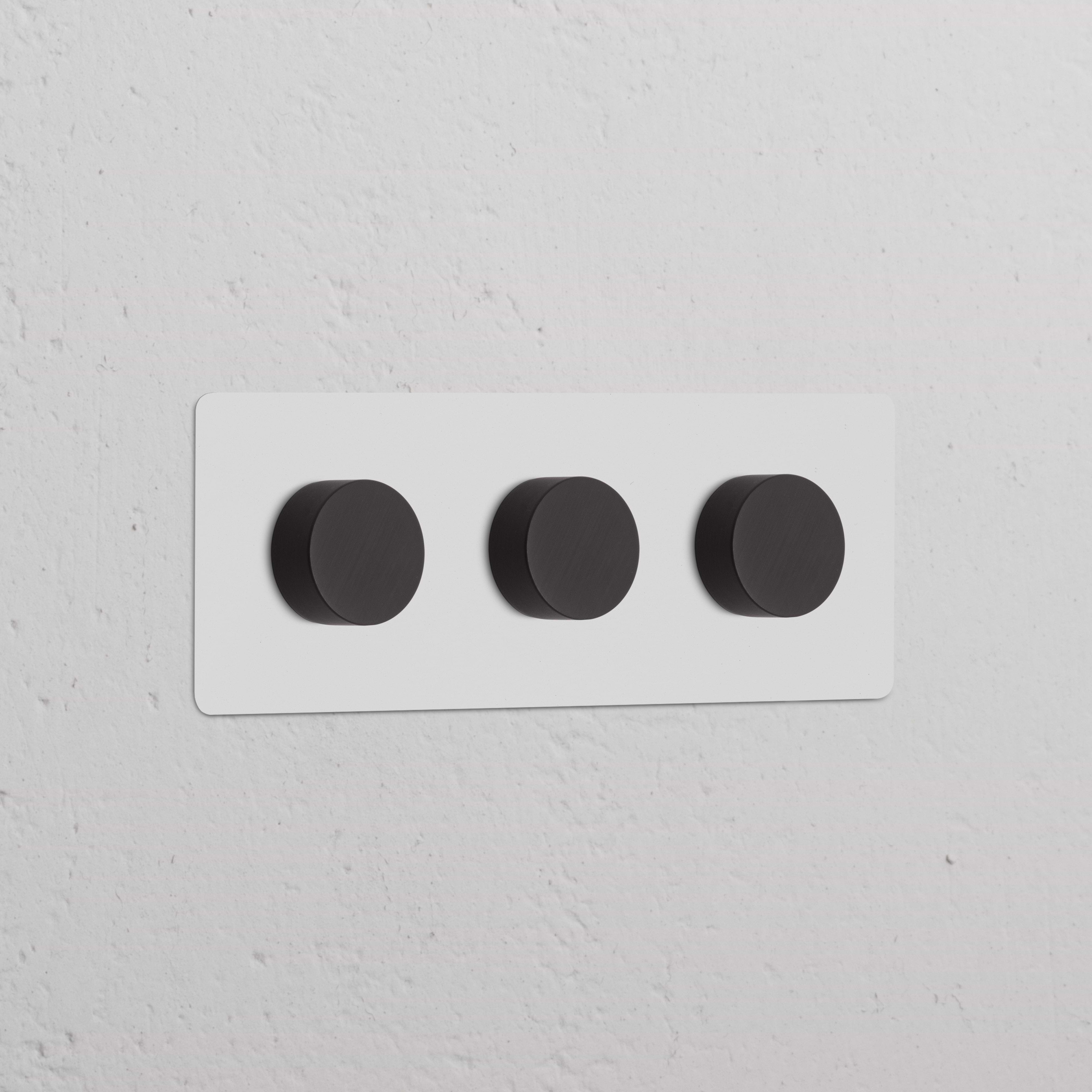 Interruptor regulador de luz multidireccional x3 en marco triple, pintable y bronce, montado en pared blanca.