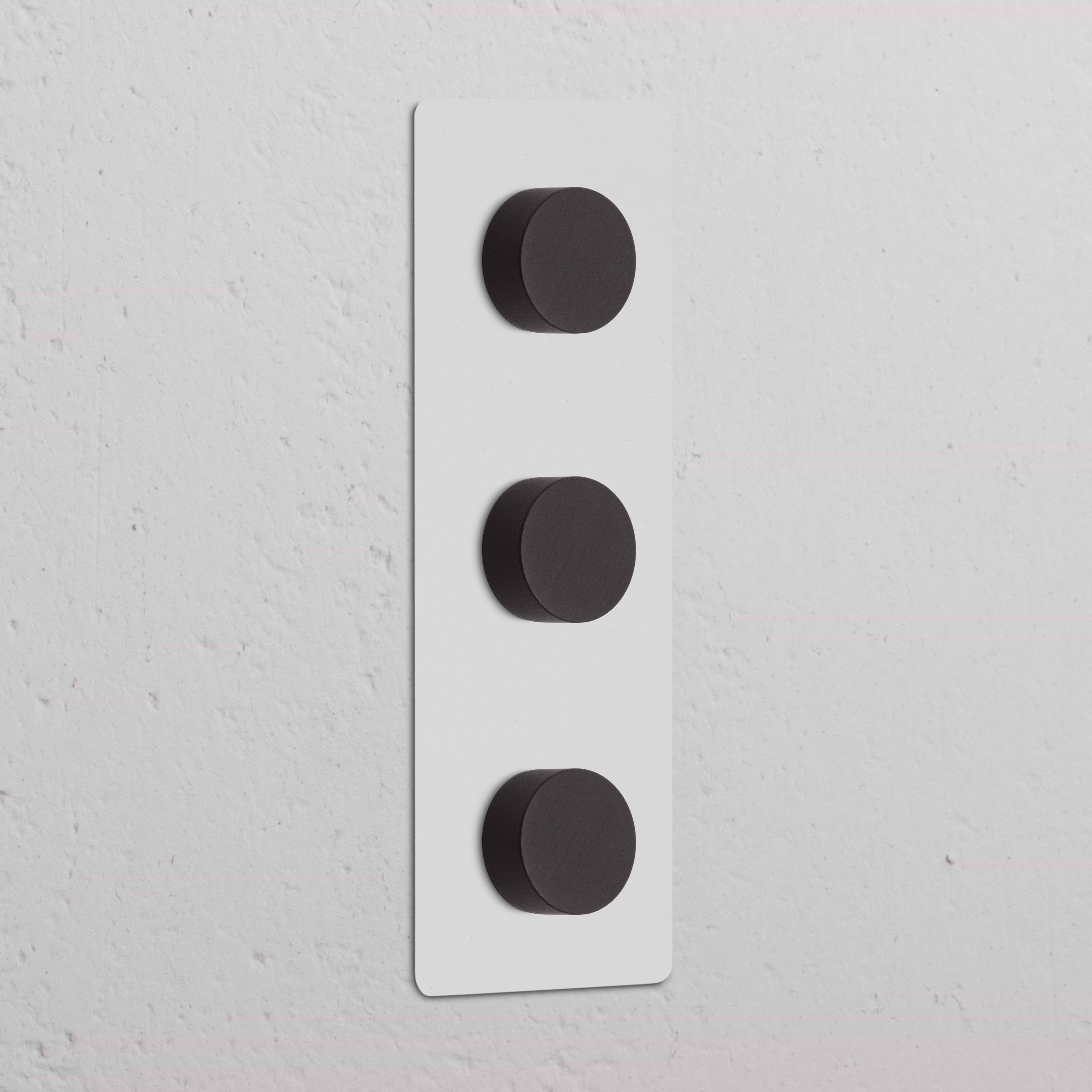 Interruptor y regulador de luz vertical triple, pintable y bronce, con tres perillas en panel rectangular blanco.