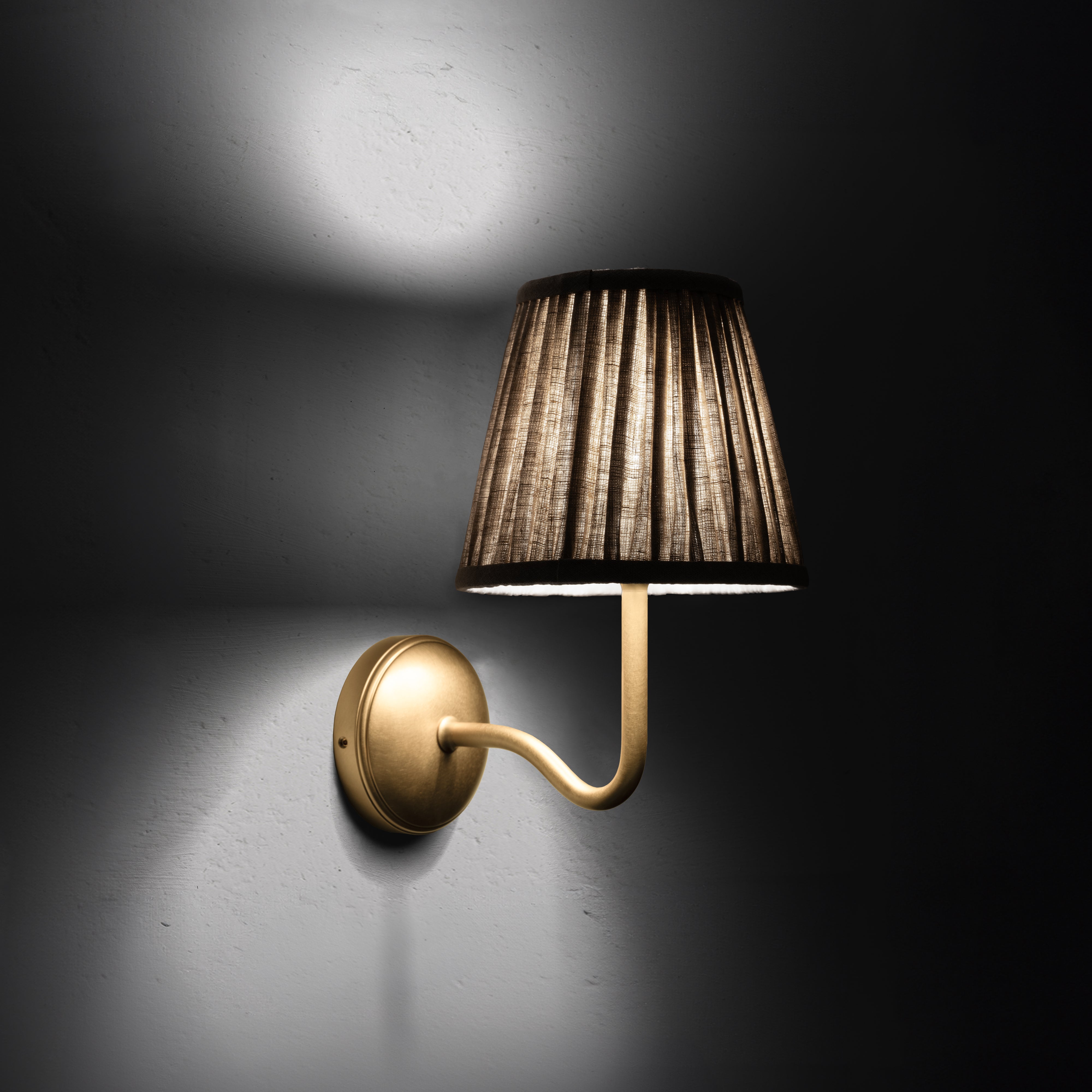 Aplique de pared Malvern mediano en beige natural colocado en ángulo y encendido, de noche