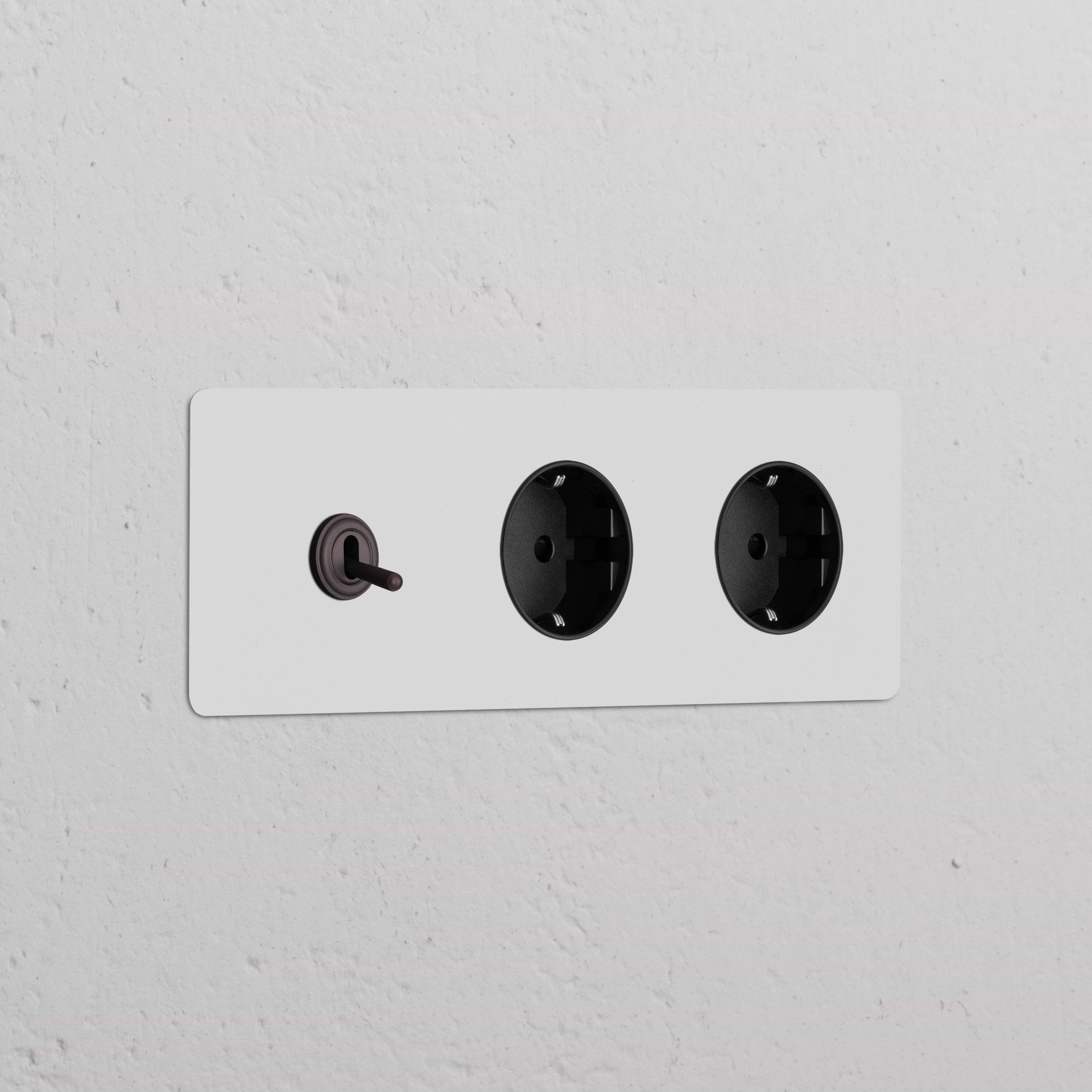 Marco triple con interruptor de palanca y dos tomas Schuko tipo F; acabado bronce pintable con insertos negros.