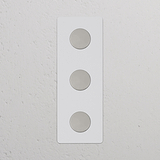 Interruptor y regulador de luz vertical triple, pintable y níquel pulido, en marco rectangular blanco.