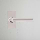Harper Poignée de Porte à Ressort à Plaque Courte en Nickel Poli sur un mur texturé blanc.