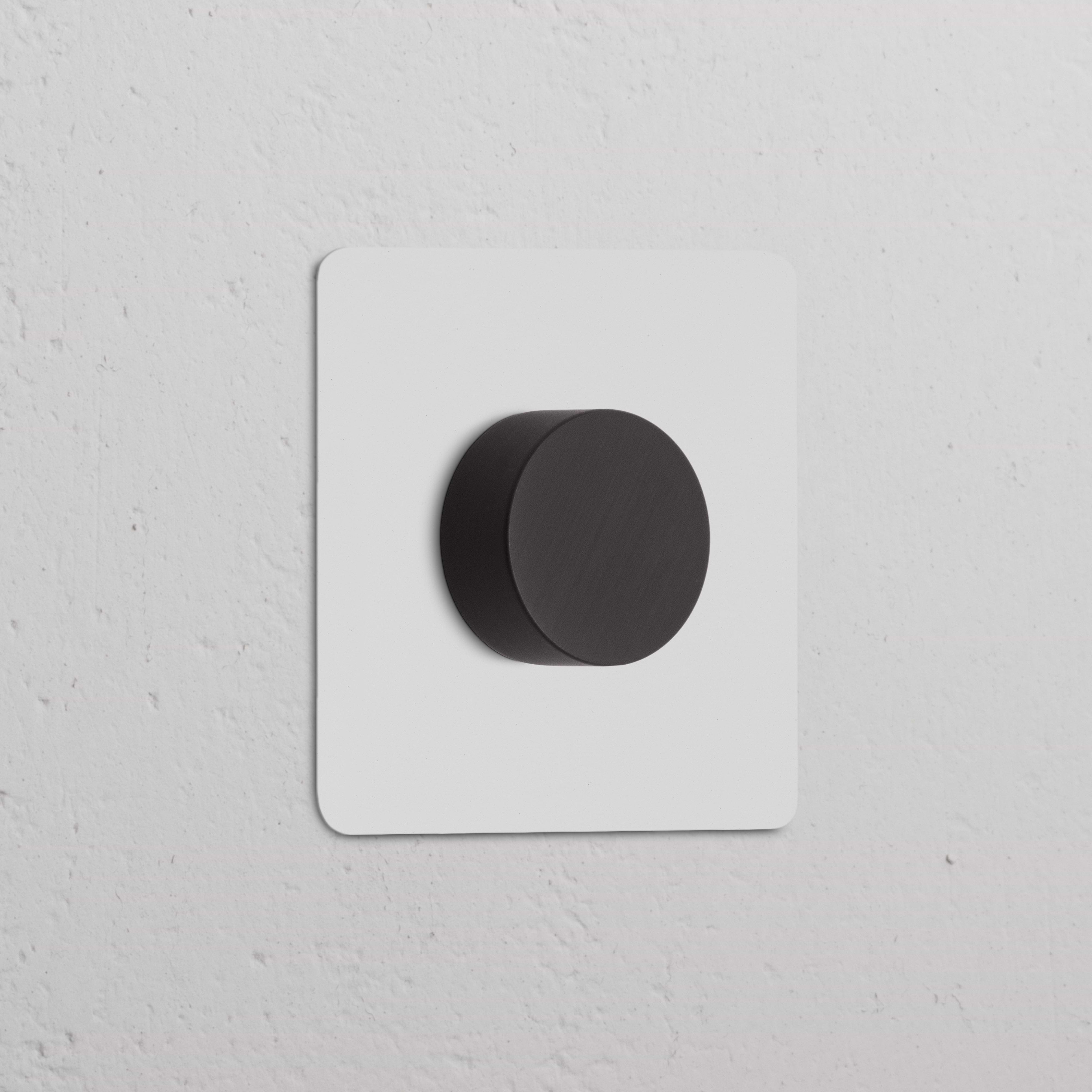 Variateur peignable en bronze (plaque simple) sur plaque blanche, monté sur un mur blanc texturé.