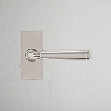 Digby Nickel Poli Poignée de Porte à Plaque Courte, élégamment polie, avec un mécanisme à ressort sur un mur blanc.
