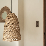 Interrupteur à levier double 2x vertical en Bronze fixé sur un mur crème avec des éléments en osier de bois qui complètent le produit fini. 