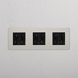 Eleganti prese elettriche Modulo Triplo 6x Bipasso nere in Nichel Lucido Nero su una parete bianca.
