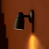 Faretto Incassato Ealing in Bronzo, montato a parete illumina verso il basso da un muro di pietra terracotta.