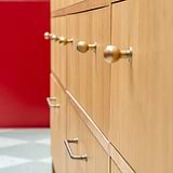 Pomello per Mobili Bayswater in Ottone Antico montato su più porte di armadietti in legno piccoli con parete rossa e pavimento piastrellato.