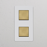Pannello interruttori a doppio bilanciere bianco con finitura in ottone anticato, design verticale; 'Interruttore a Bilanciere Doppio Verticale'.