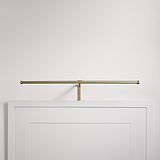 Harrow Applique per Quadri da 580 mm in Ottone Antico, elegantemente montata sopra una cornice vuota su una semplice parete bianca.