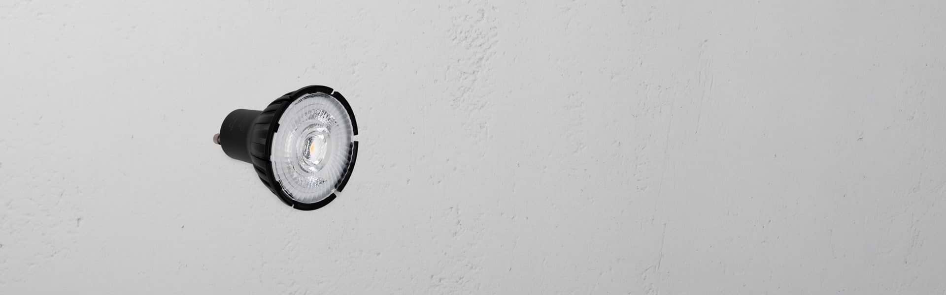 Close-up of a round LED bulb with a black base, mounted on a textured white wall.