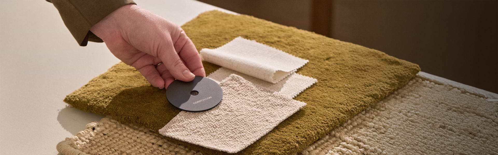 A hand selects a circular color swatch from a display of textured fabric samples in earthy tones and neutral shades.