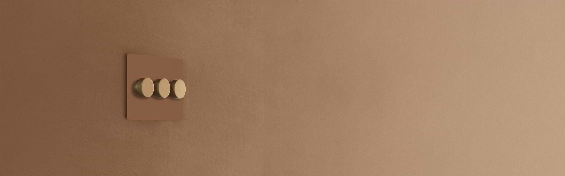 A modern light switch with three round gold dimers on a matte brown wall, showcasing sleek minimalist design.