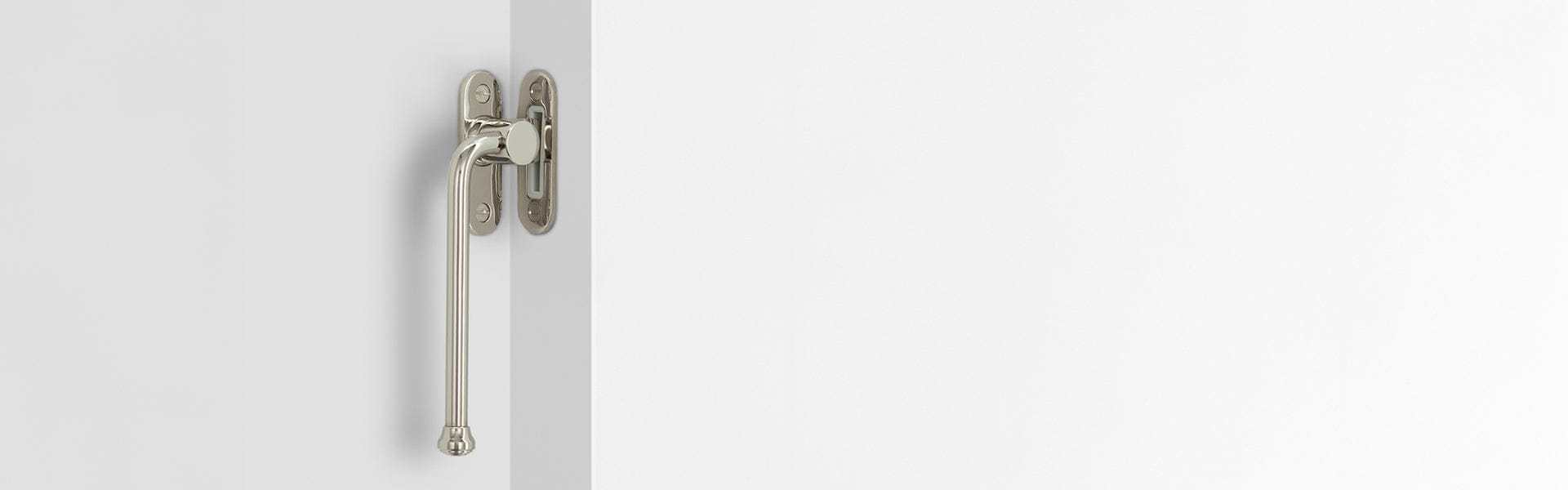 Close-up of a polished nickel window fastener attached to a white wall corner, showcasing its sleek design and fastening.