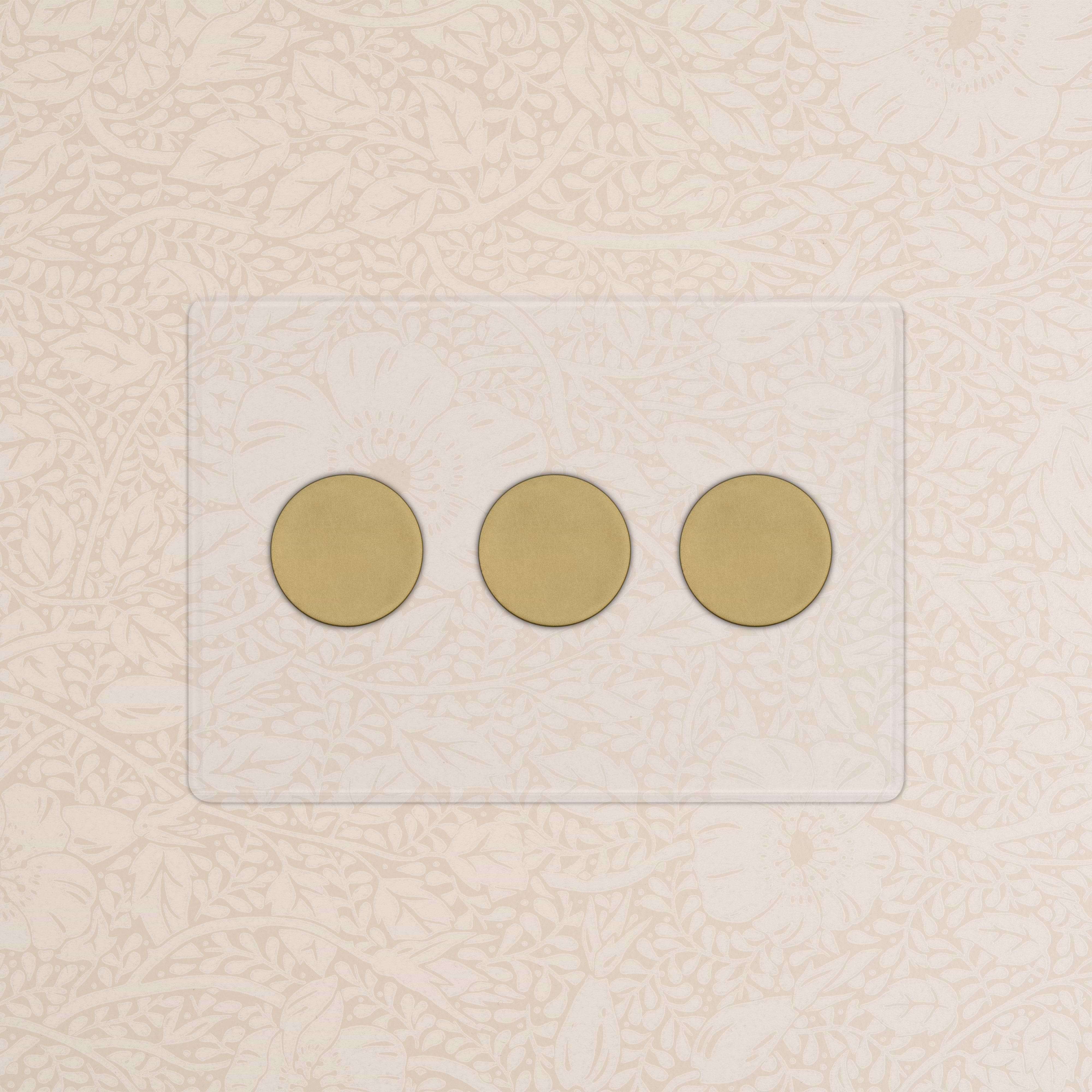 Kew 3G Dimmer Switch in clear antique brass with three round dials on a cream floral patterned wall.