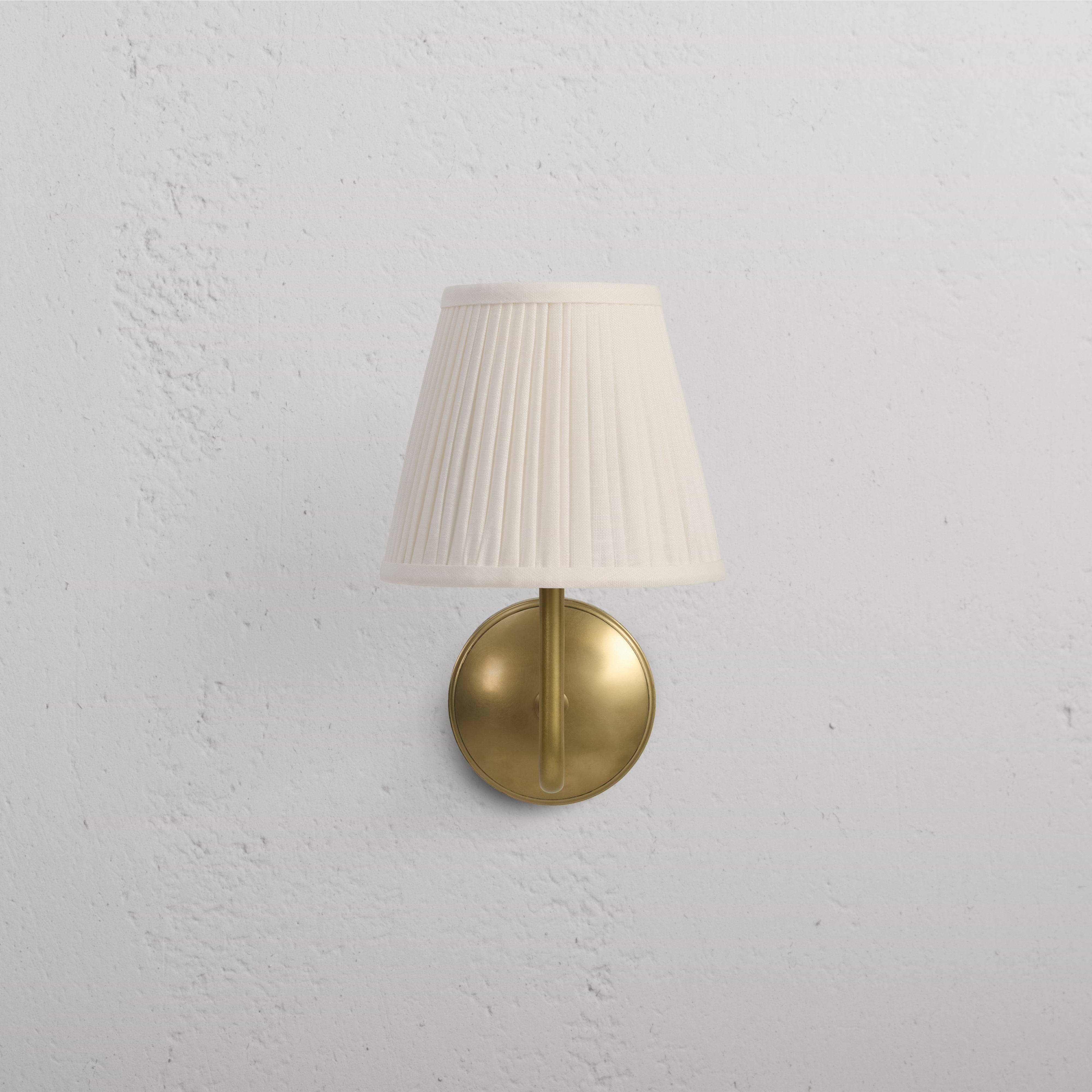 Malvern Medium Wall Light in Alabaster White with antique brass base and pleated white lampshade on wall.