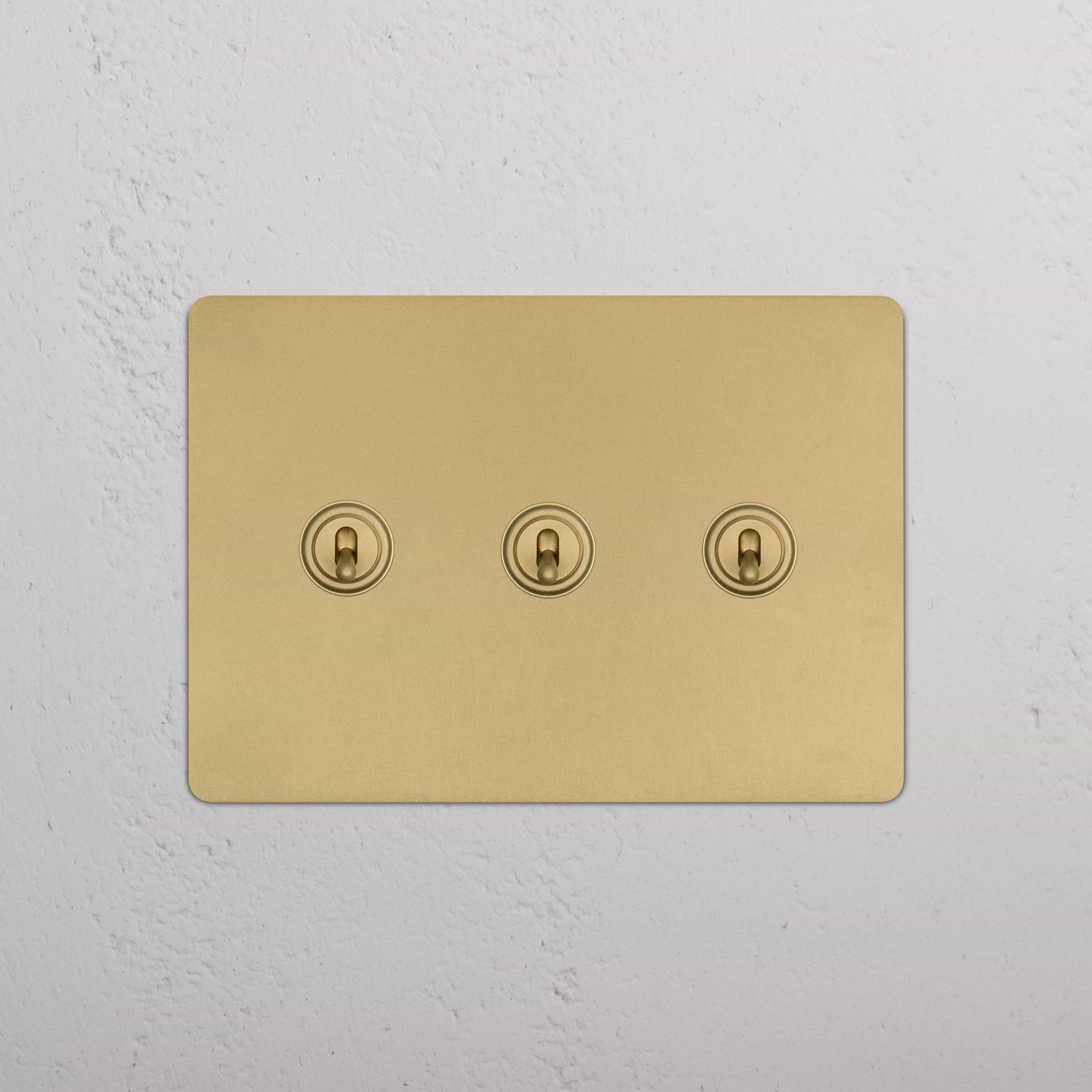 Kew 3G Toggle Switch in antique brass finish featuring three round toggles, mounted on a wall.