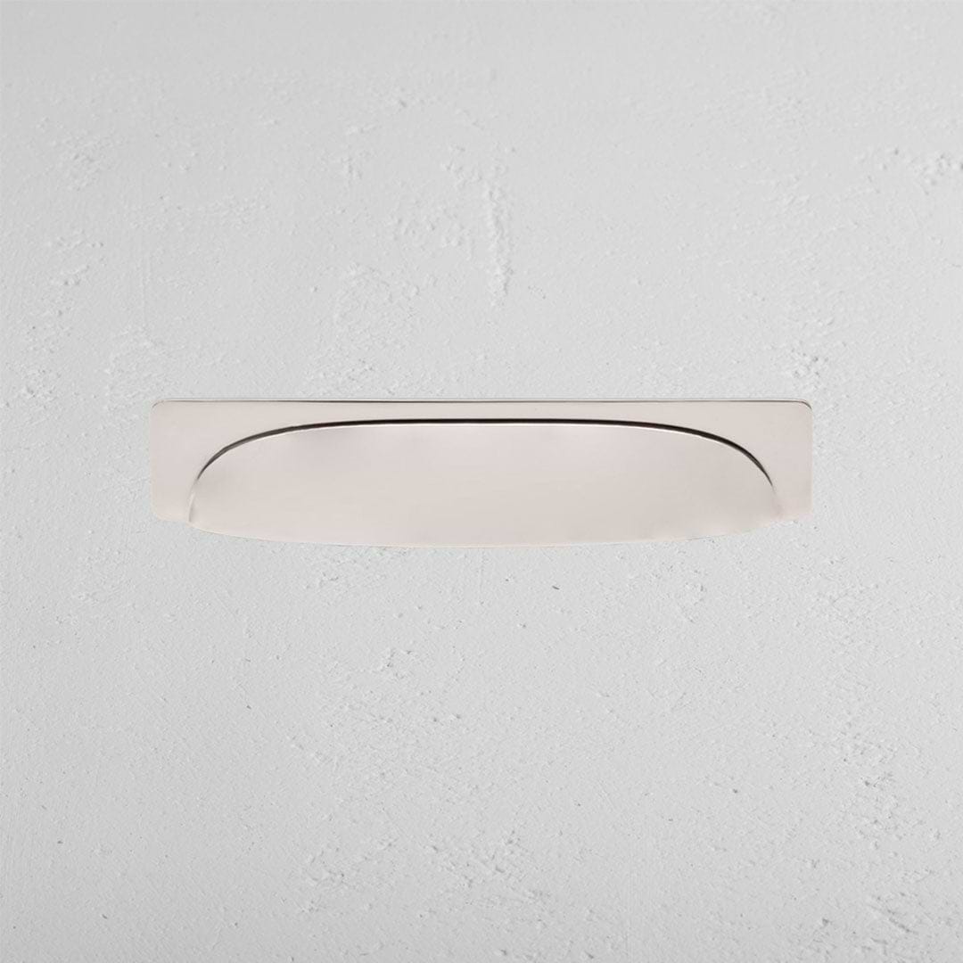 Elm Cup Handle Medium in polished nickel, curved and recessed, mounted on a white textured wall.